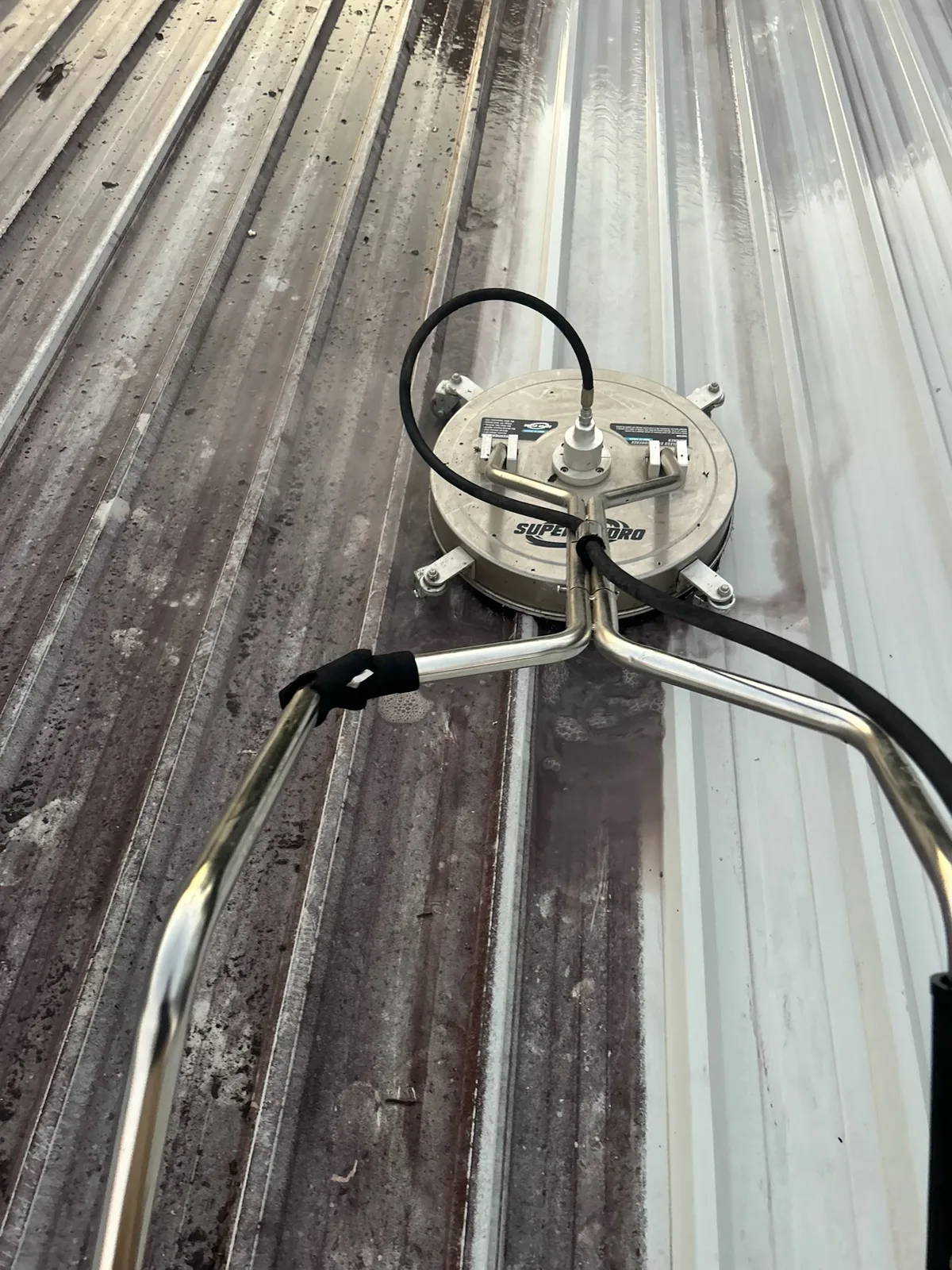 A surface cleaner in use on a corrugated metal roof